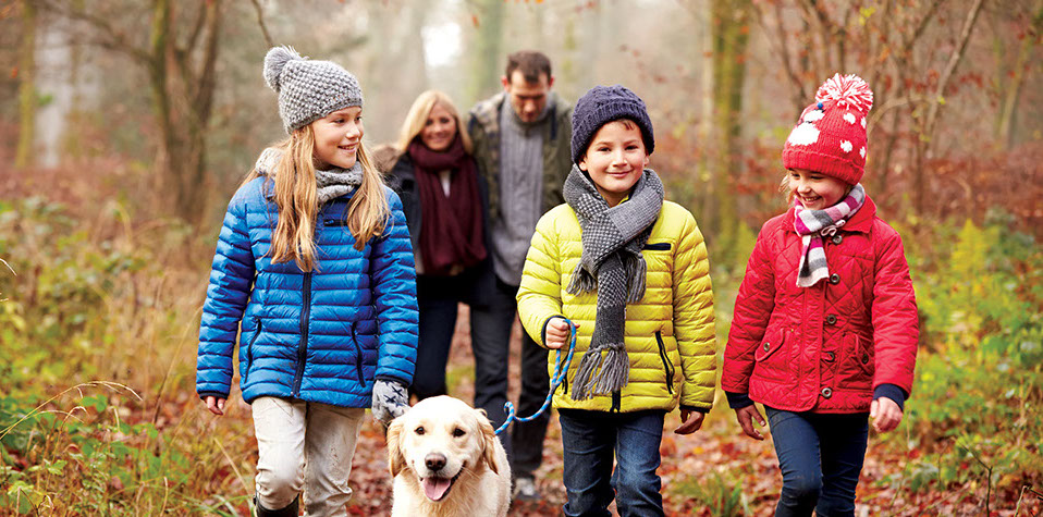 Family with winter coats walking in the forest with their white labrador dog
